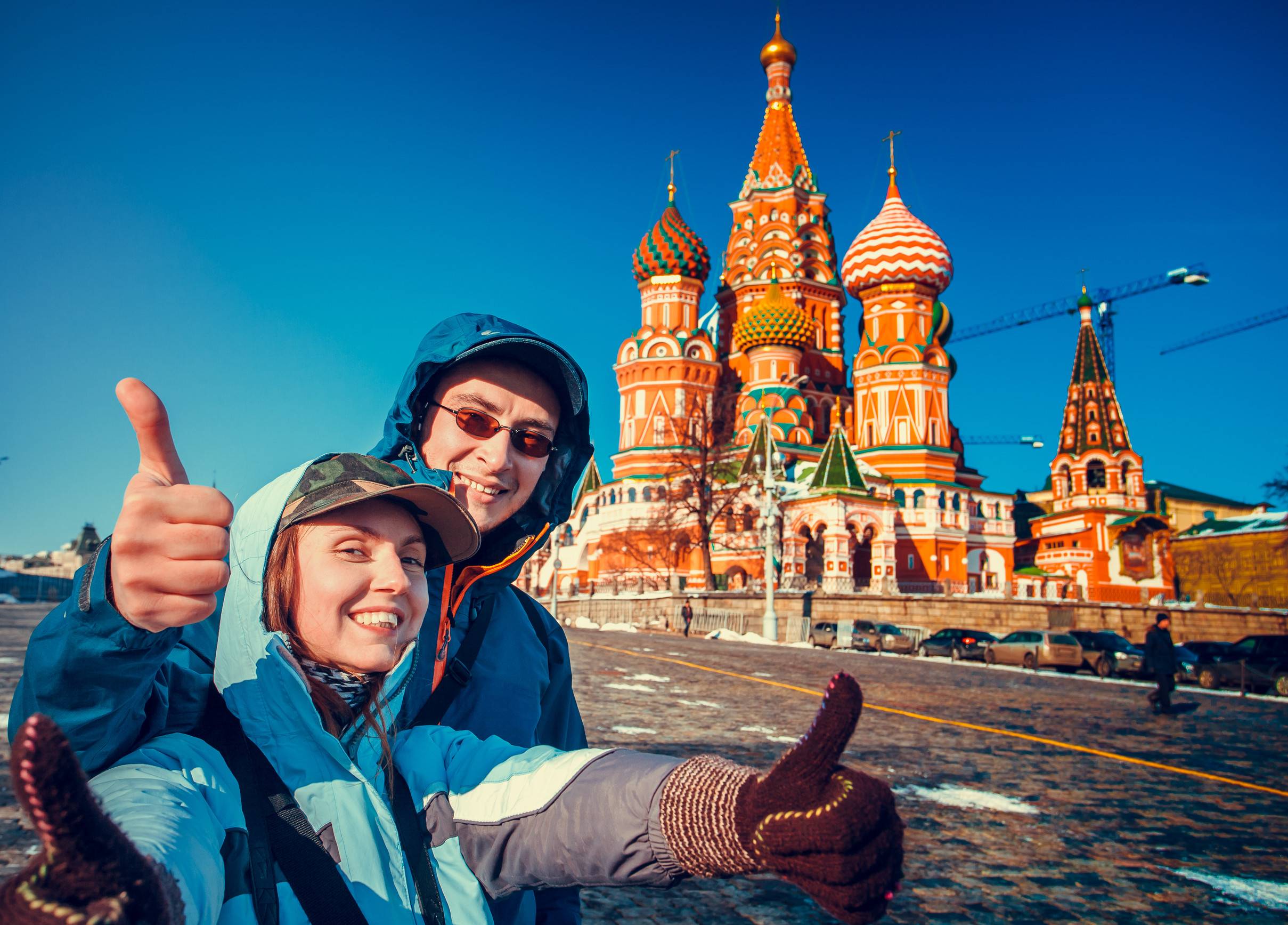 Happy tourists sightseeing city with fingers up next to Saint Basil's Cathedral, Red Square, Moscow